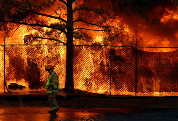 A captain with the Fulton County fire department walks past a fire at a carpet warehouse