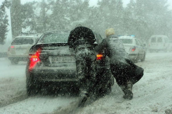 Athens, Greece: A couple push their car during heavy snowfall