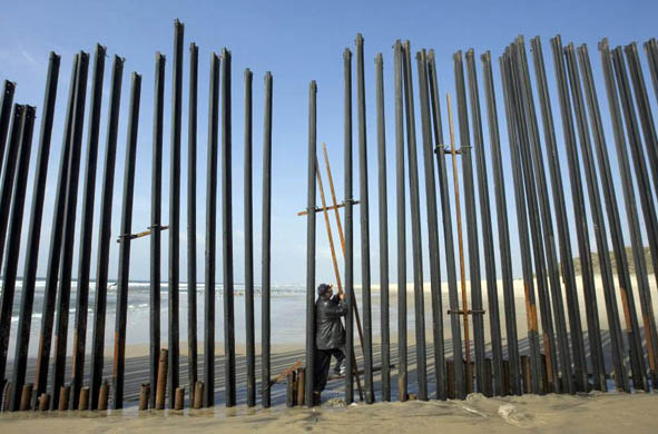 A man stands in the middle of the border fence dividing Mexico and the US