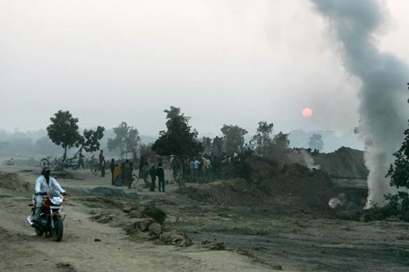 Satgram, India: A villager rides a motorcycle past smoke coming out of an underground mine fire