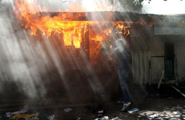 A resident puts out the fire of a house ignited by protestors