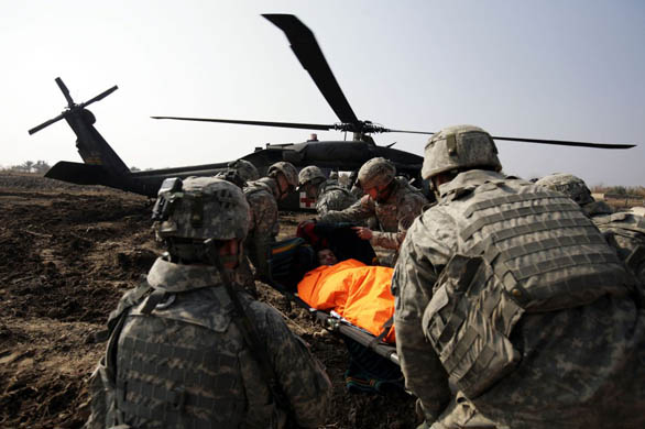 US army soldiers carry a local citizen injured in a booby-trapped house to a waiting medivac helicopter