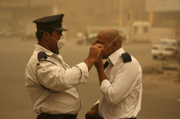 Baghdad, Iraq: A police officer helps his colleague put on a mask during a sandstorm