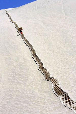 Dunhuang, China: A worker carries wood up a dune in the desert