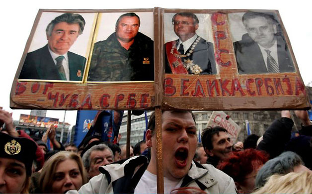 February 2006, Belgrade, Serbia: A Radical party supporter holds photos of war crimes suspects Radovan Karadzic, Ratko Mladic and Vojislav Seselj at a rally