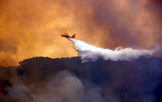 Rhodes, Greece: A firefighting aircraft battles a wildfire burning in a forest