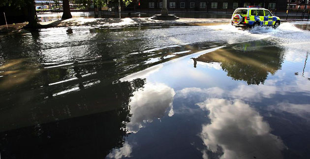 London, UK: A police car drives through a pool of water on a flooded road outside the Oval tube station