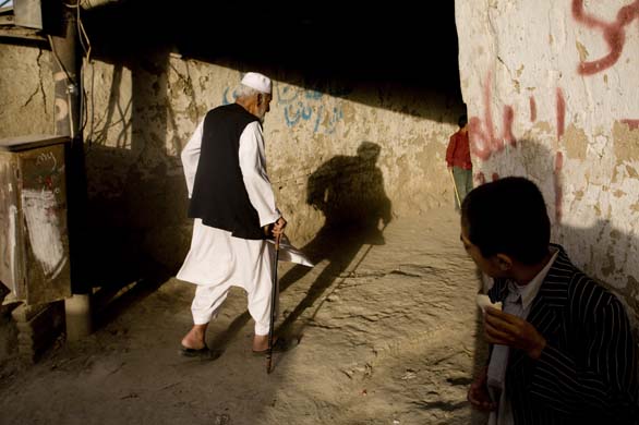 A young boy watches an elderly gentleman makes his way though an alley in Kabul  