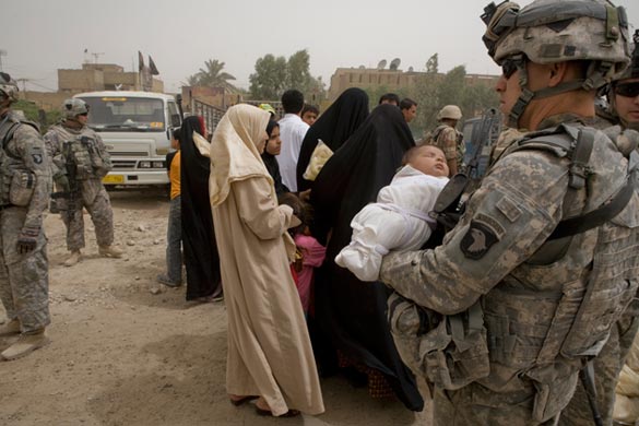 A US soldier from the 101st Airborne Division holds a baby while the mother collects food distributed by US troops in Shulla, north-west Baghdad
