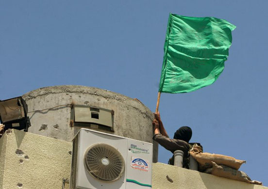 A Hamas militant places a green Islamic flag on a guard tower as they celebrate their capture of the Fatah headquarters from Fatah