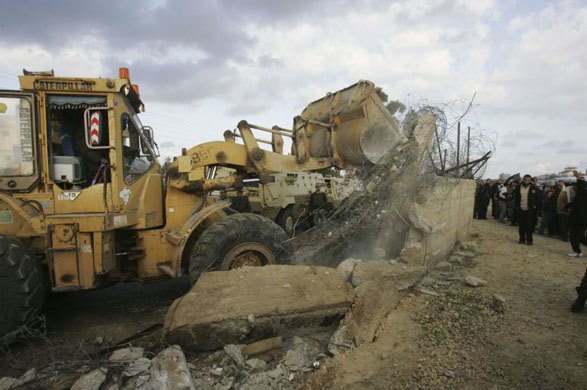 A bulldozer destroys part of a border wall as Palestinians cross the border into Egypt