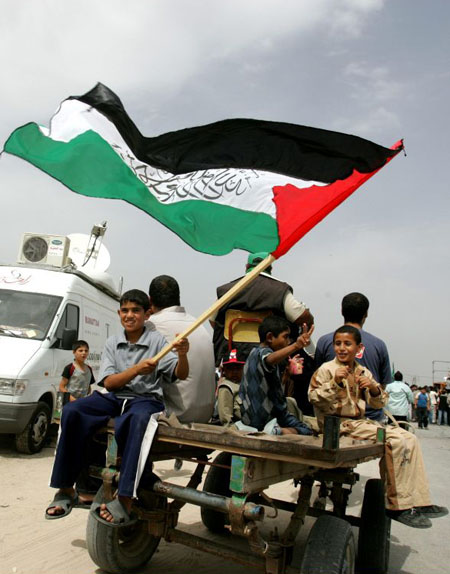 Young Hamas supporters ride a horse cart while one of them waves his national flag at a protest 