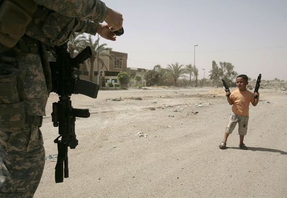 Baghdad, Iraq: A child armed with plastic toy weapons, approaches a US soldier on patrol in the Sadr city district