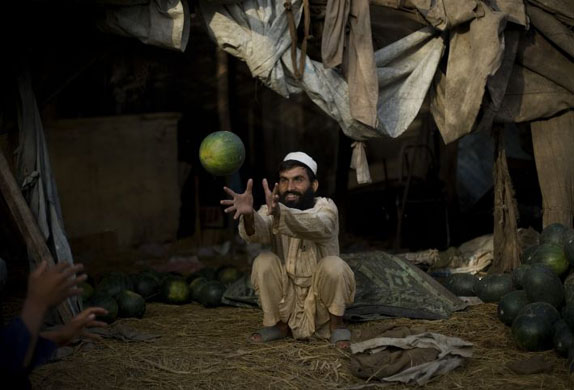 Islamabad, Pakistan:  A market trader catches a watermelon at his stall on the outskirts the city. Photograph: Photograph: Emilio Morenatti/AP