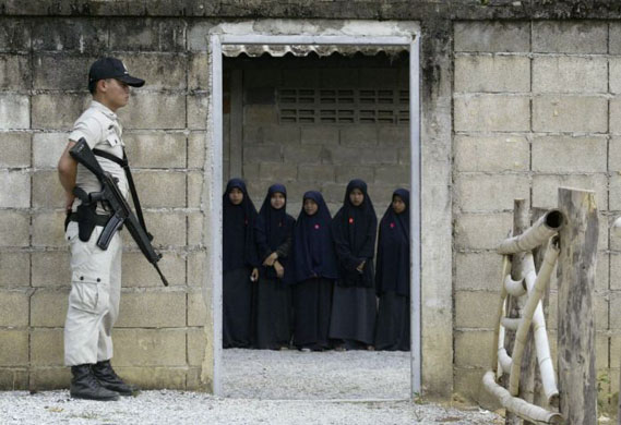 Yala, Thailand: A policeman stands guard as female students await the arrival at their school of the former  prime minister of Thailand, Surayud Chulanont. Photograph: Surapan Boonthanom/Reuters