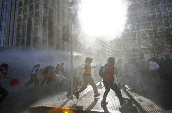 Santiago, Chile: Students take cover from police water cannon during a rally protesting against proposed education reforms. Photograph: Ivan Alvarado/Reuters