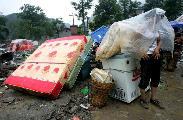 Beicuan County, China: An earthquake survivor shields herself from the rain with plastic cloth as she waits for transportation