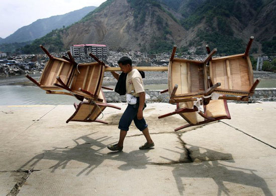 Beichuan county, China: A resident carries his furniture past buildings destroyed by the May 12 earthquake and flooding