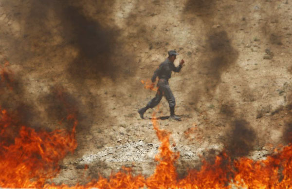 Kabul, Afghanistan: A policeman walks behind a pile of burning narcotics