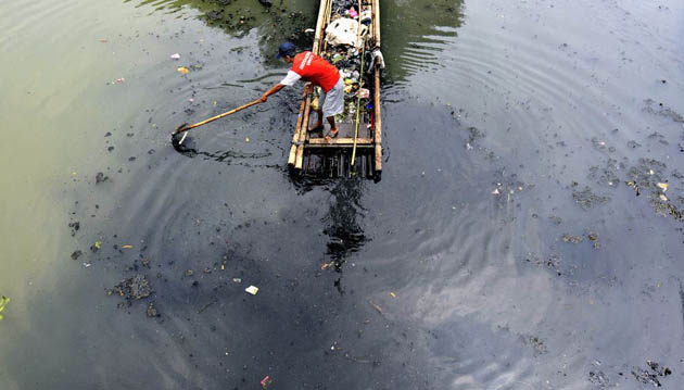A scavenger collects polythene and other recyclable items from a polluted canal