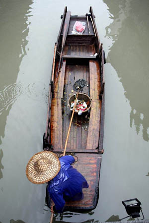 Wuzhen, China: A worker collects debris along a canal