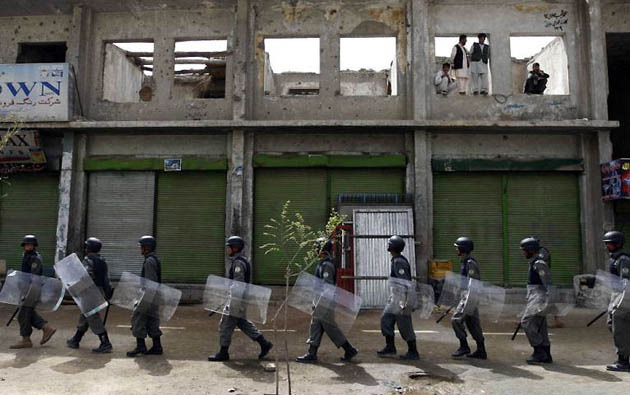 Kabul, Afghanistan: Riot policeman patrol as people watch a demonstration