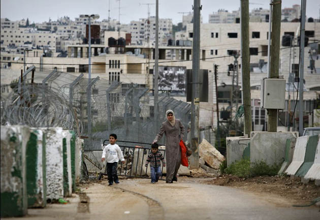of A-Ram, West Bank: A Palestinian woman walks with her children through an Israeli military checkpoint