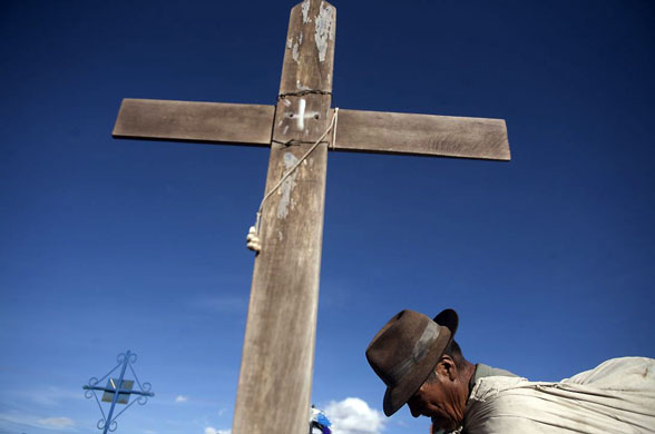 El Alto, Bolivia: A poor man prays by the tomb of an Aymara Indian in exchange for food during Day of the Dead celebrations