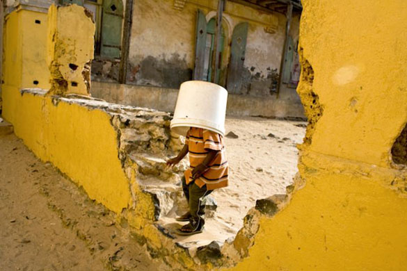 Goree Island, Senegal: A boy with a bucket on his head tries to walk through a hole in a wall