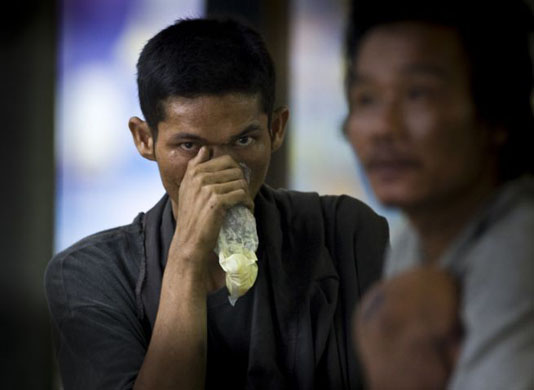 A beggar sniffs glue while sheltering from the monsoon rain   in Bangkok 