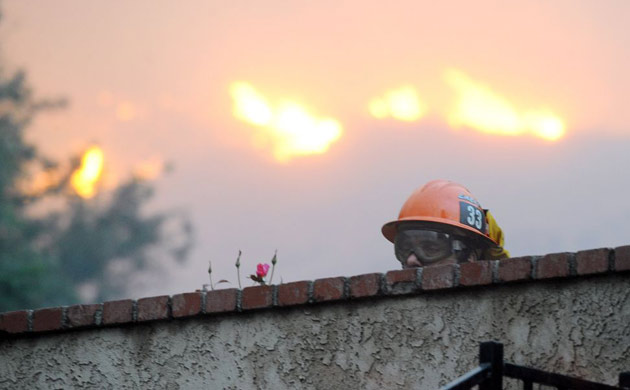 A firefighter looks over a backyard wall as he and his team protect homes against arriving wildfire, in the Knollwood section of Los Angeles