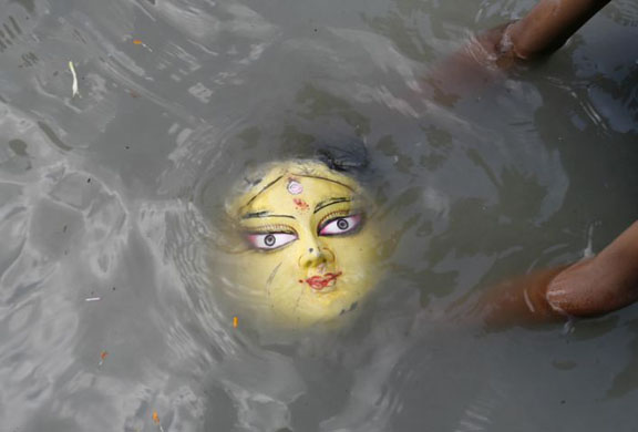 A devotee immerses an idol of Hindu goddess Durga into the waters of river Mahananda 