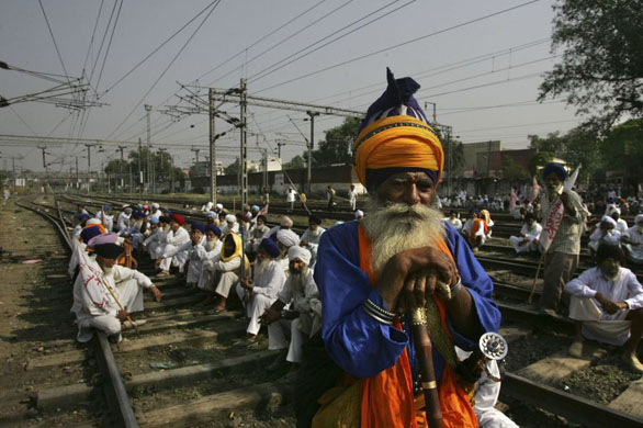 Amritsar, India: A Sikh farmer dressed as a warrior stands as other farmers sit on railway tracks during a protest against state and central governments