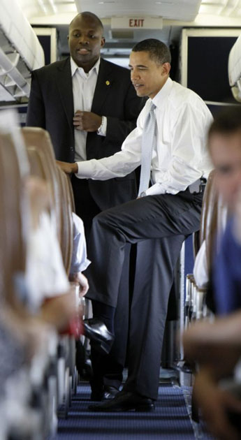 Barack Obama talks with Reggie Love, on his campaign charter plane before takeoff in Washington