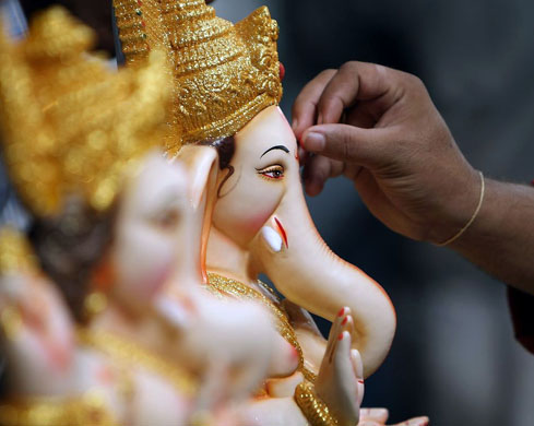 Mumbai, India: A Hindu puts a dab of vermillion on an idol Lord Ganesha