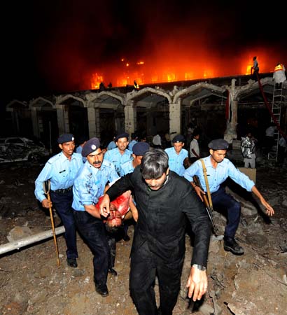 Pakistani policemen carry the body of a blast victim outside the burning facade of the Marriott hotel