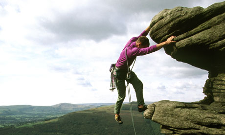 A man climbs a rock at Bamford in Derbyshire, England, UK
