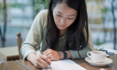 Mid adult woman writing on paper in cafe