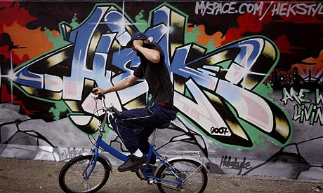 A boy covers his face as he cycles past graffiti painted on the Thames tidal