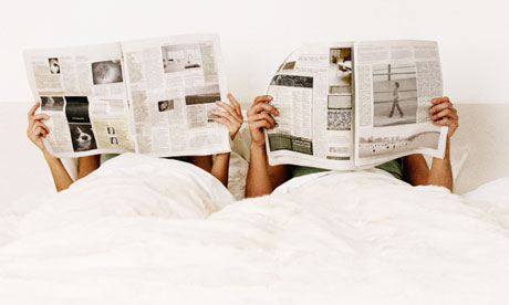 Couple lying in bed holding up newspapers