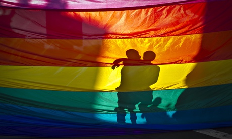 Men embrace behind a rainbow flag.