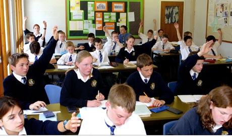 Junior school children in classroom with raised hands