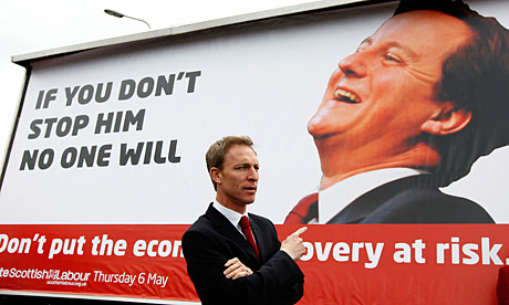 Secretary of state for Scotland Jim Murphy gestures towards a poster of David Cameron, in Edinburgh.