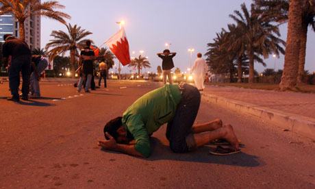 A Bahraini protester prays in the street in front of tanks