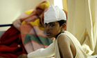An injured boy sits on his bed in a loca