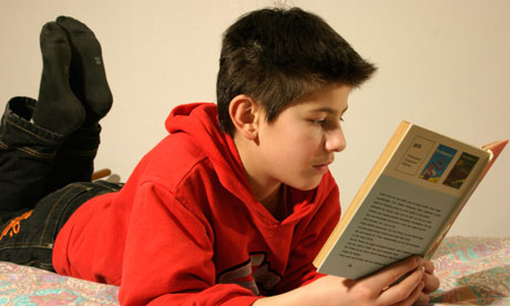 A young boy lying on his bed reading a book