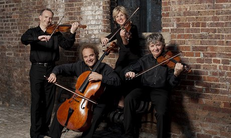 The Takács Quartet - sitting, bows on strings and smiling broadly