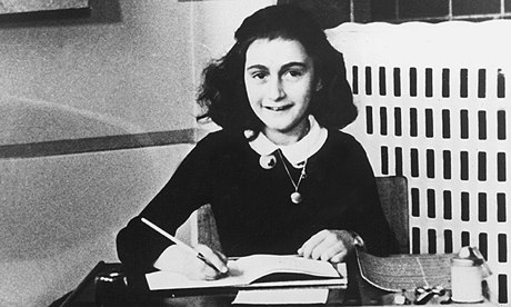 Anne Frank photographed at a desk with pen in hand