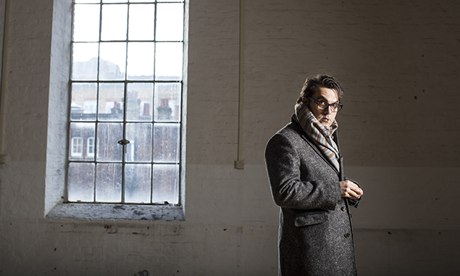 Joe Wright in a bare room wearing scarf and overcoat