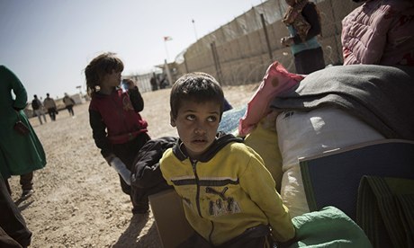 A Syrian boy sits with his family's belongings in a refugee camp